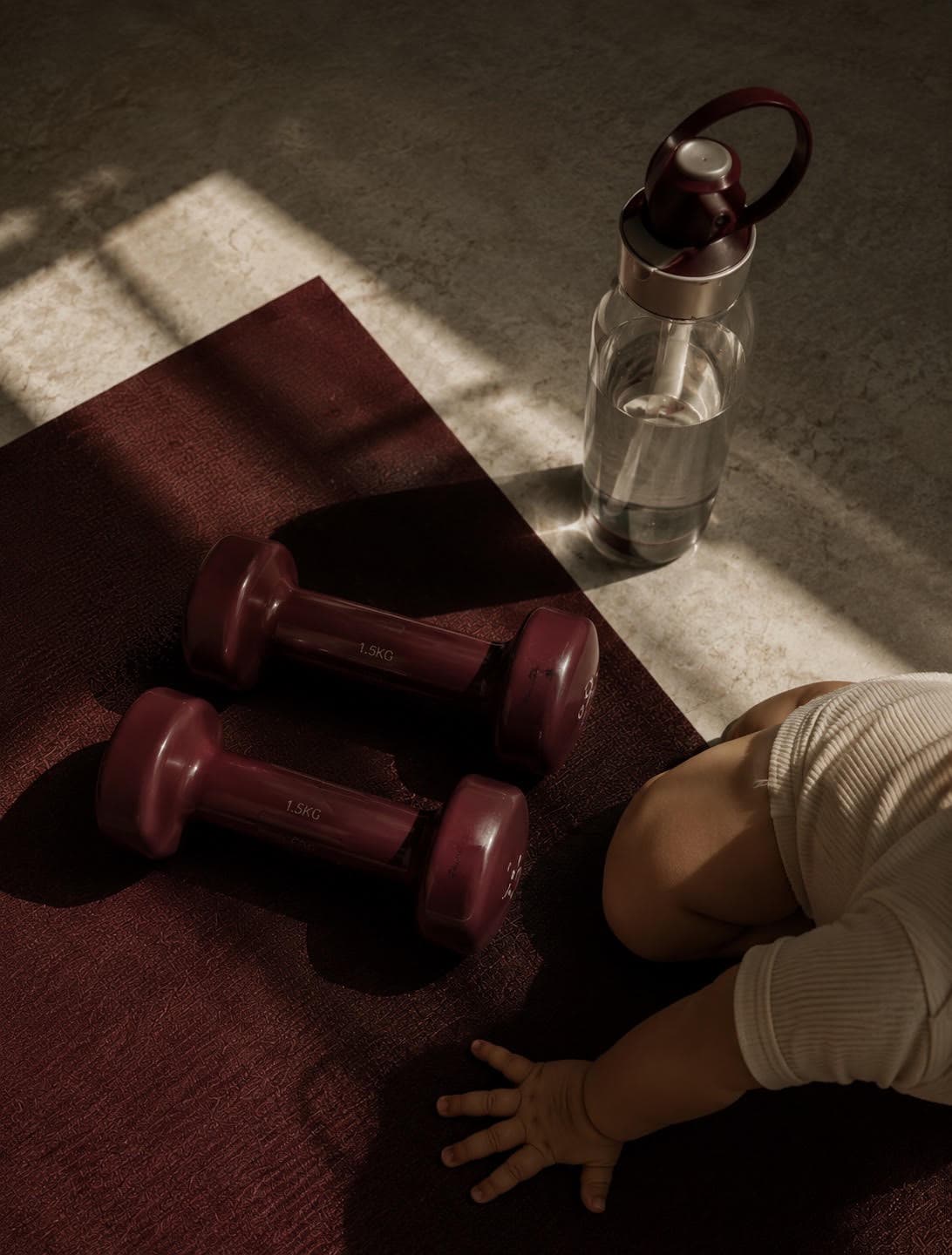 Baby beside dumbbells and water bottle on a maroon yoga mat